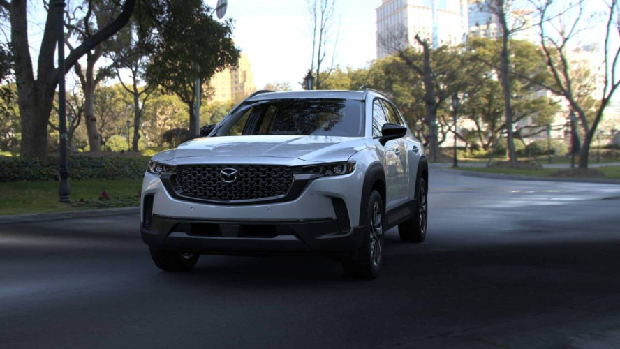 A white Mazda CX-50 Hybrid driving down the road.