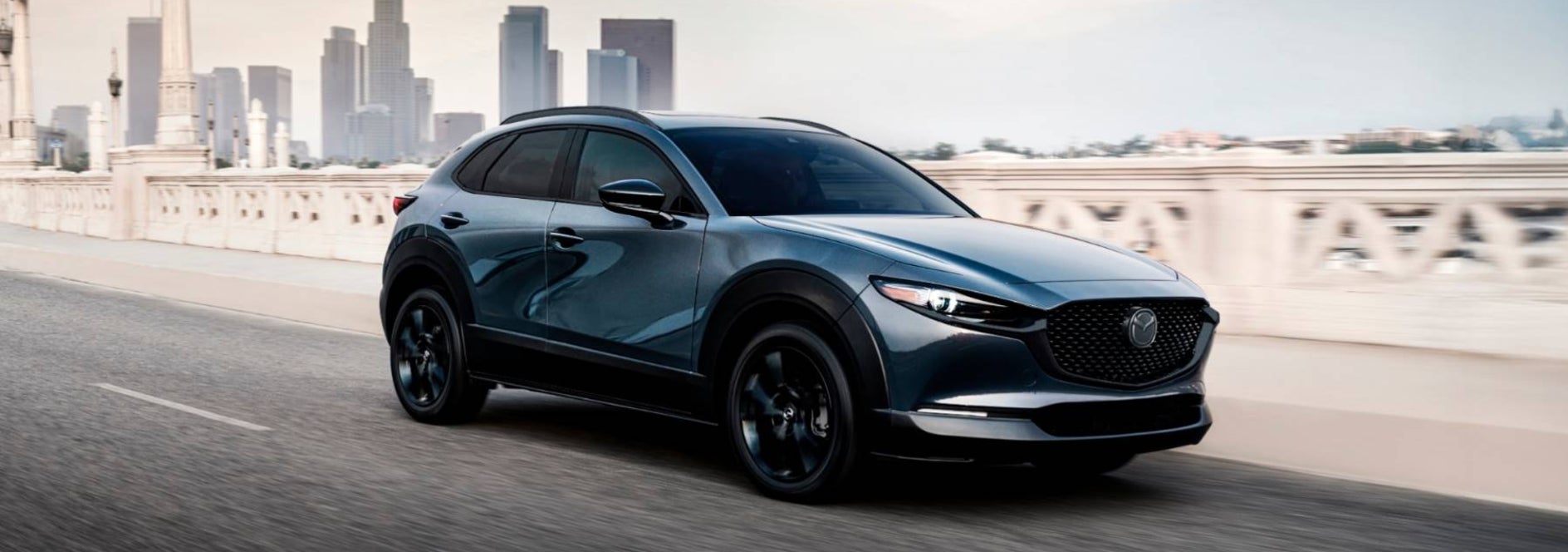 A dark blue Mazda CX-30 driving over a bridge away from a city.