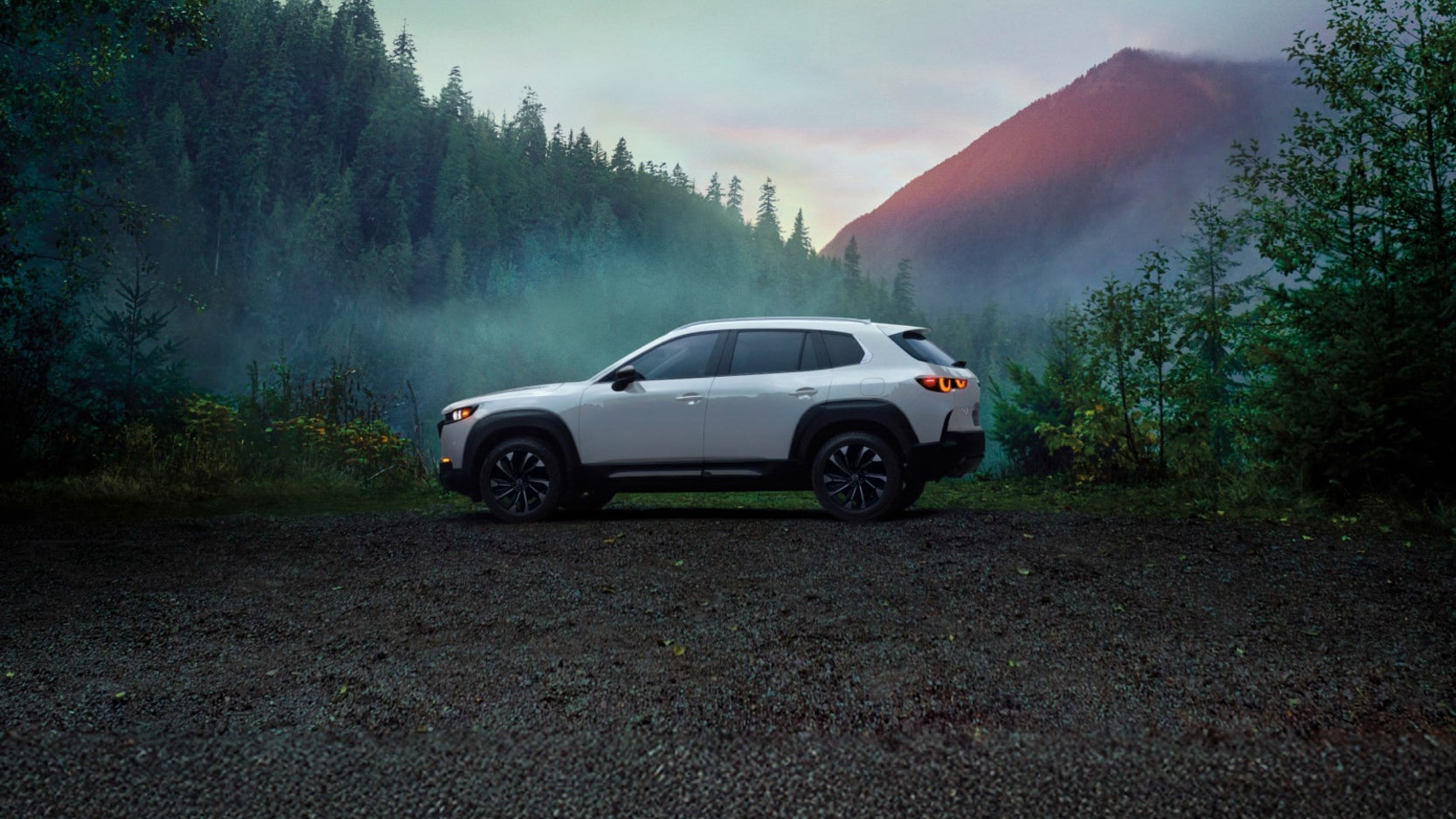 A white Mazda CX-50 Hybrid in profile in a forest clearing.