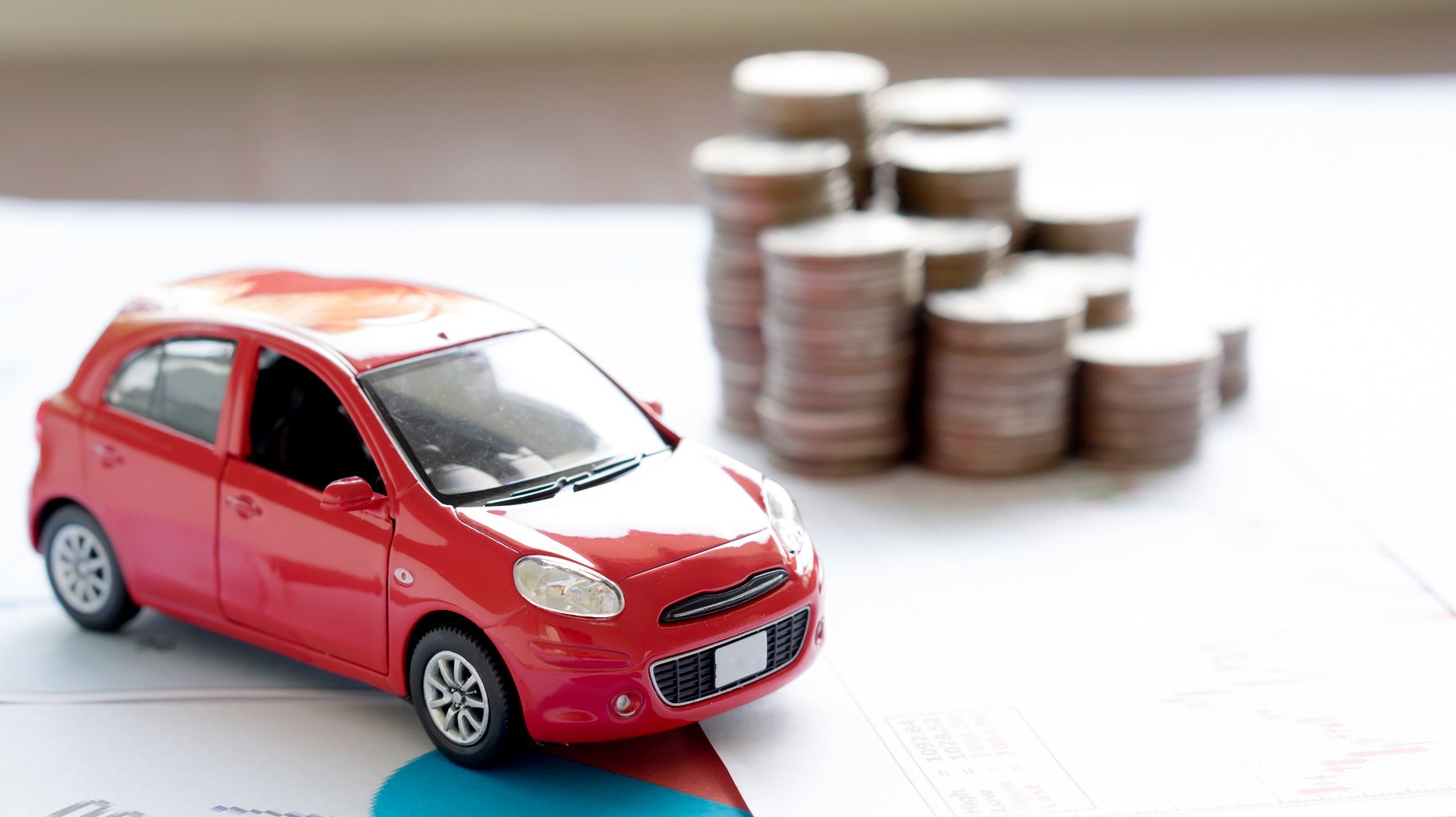 A red toy car on some documents near a stack of coins.
